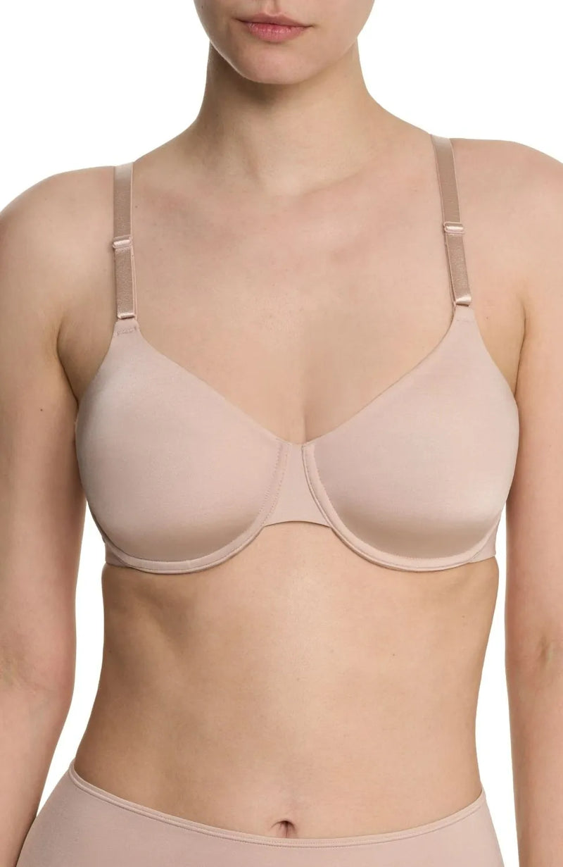 A close-up of a model wearing a seamless, underwire bra in a light nude beige color, shown from the chest up against a plain white background.